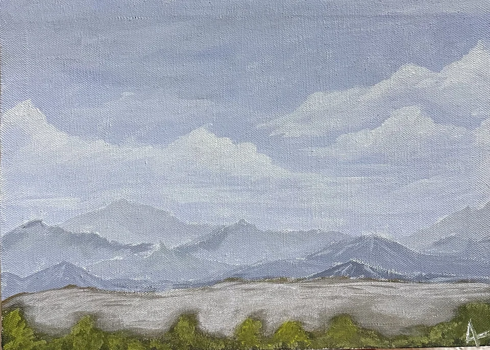 Pale city forms and green trees beneath blue-grey mountains and a broad cloudy sky.