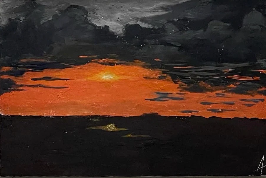 An orange sunset beneath thick black clouds above a dark landscape.